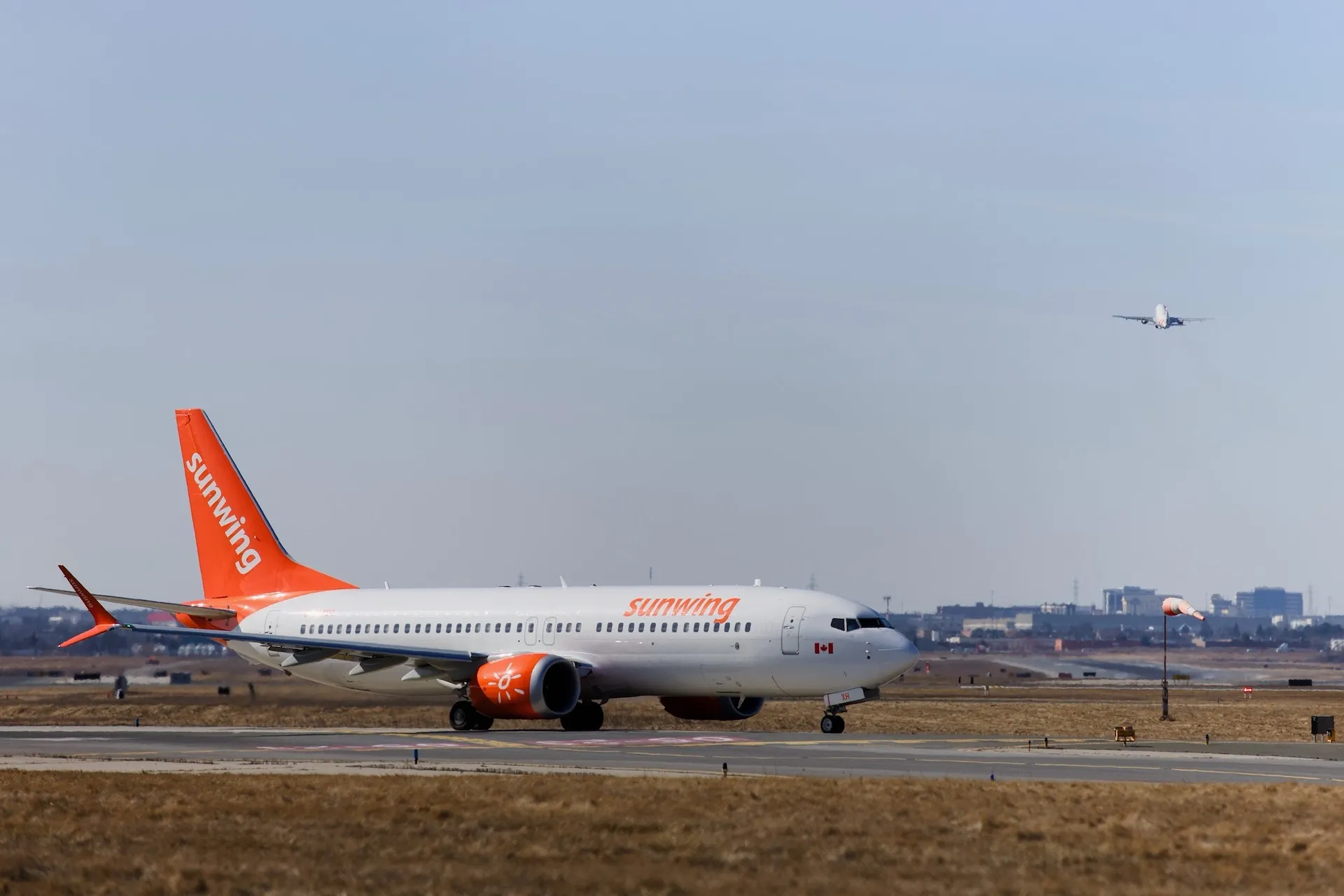 A Sunwing 737 waits at the runway while another plane takes off.