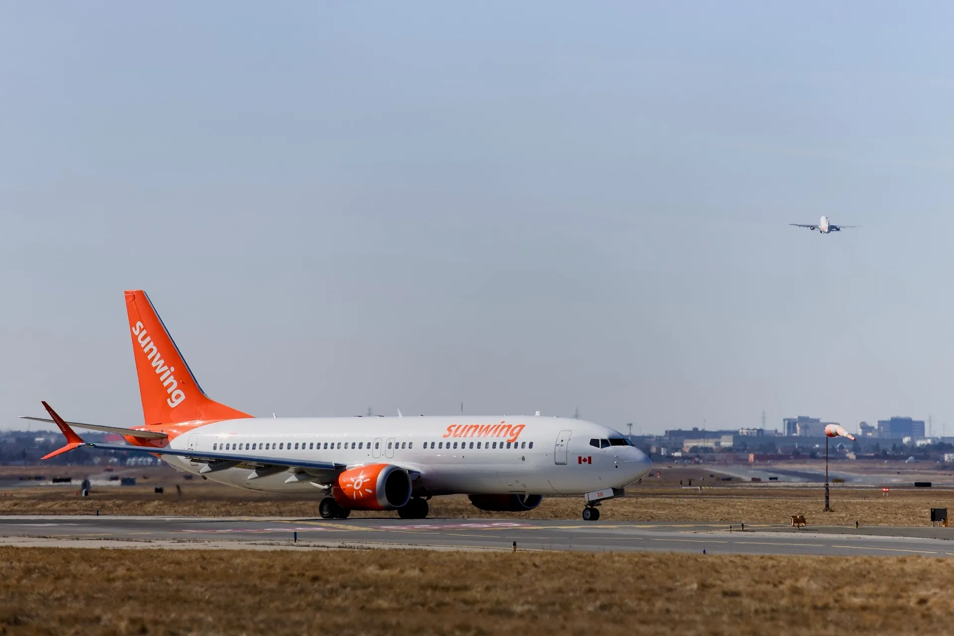 A Sunwing 737 waits at the runway while another plane takes off.